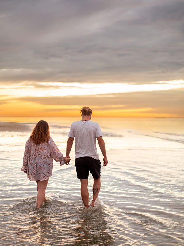 couple se tenant la main marchant dans l'eau sur la plage