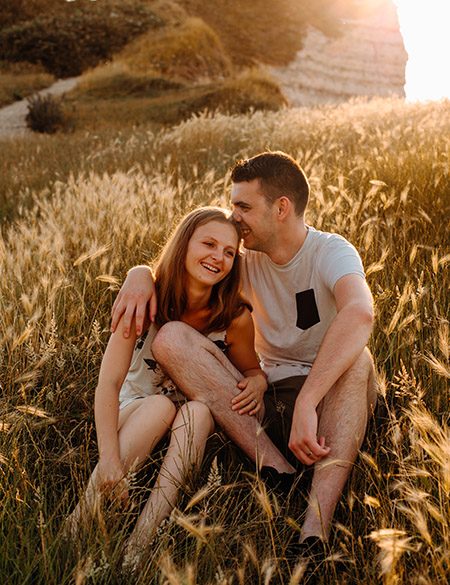 Photographie d'un couple dans les herbes de falaises d’Étretat riant ensemble
